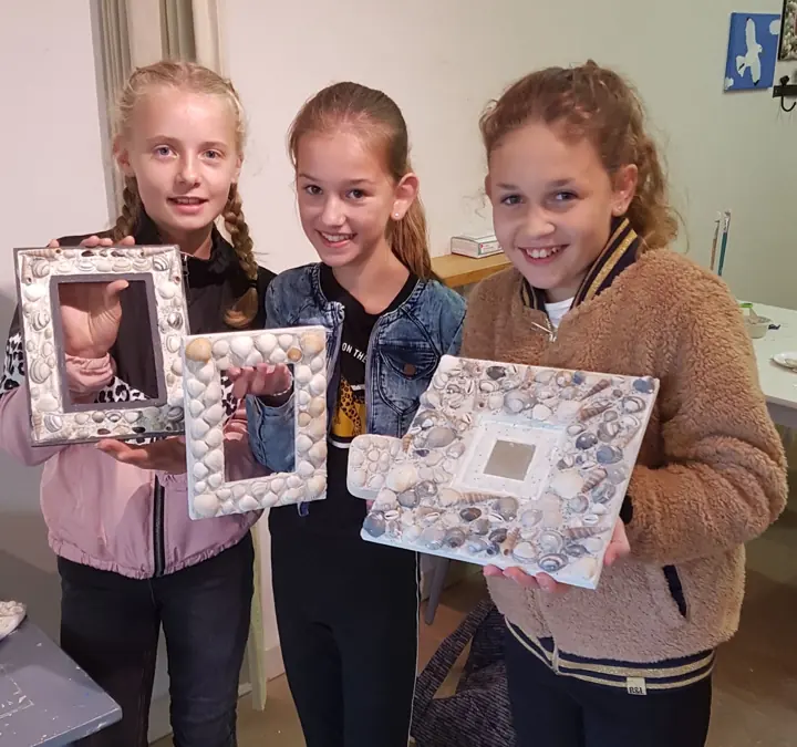 Drie meisjes laten hun schelpenmozaïek zien